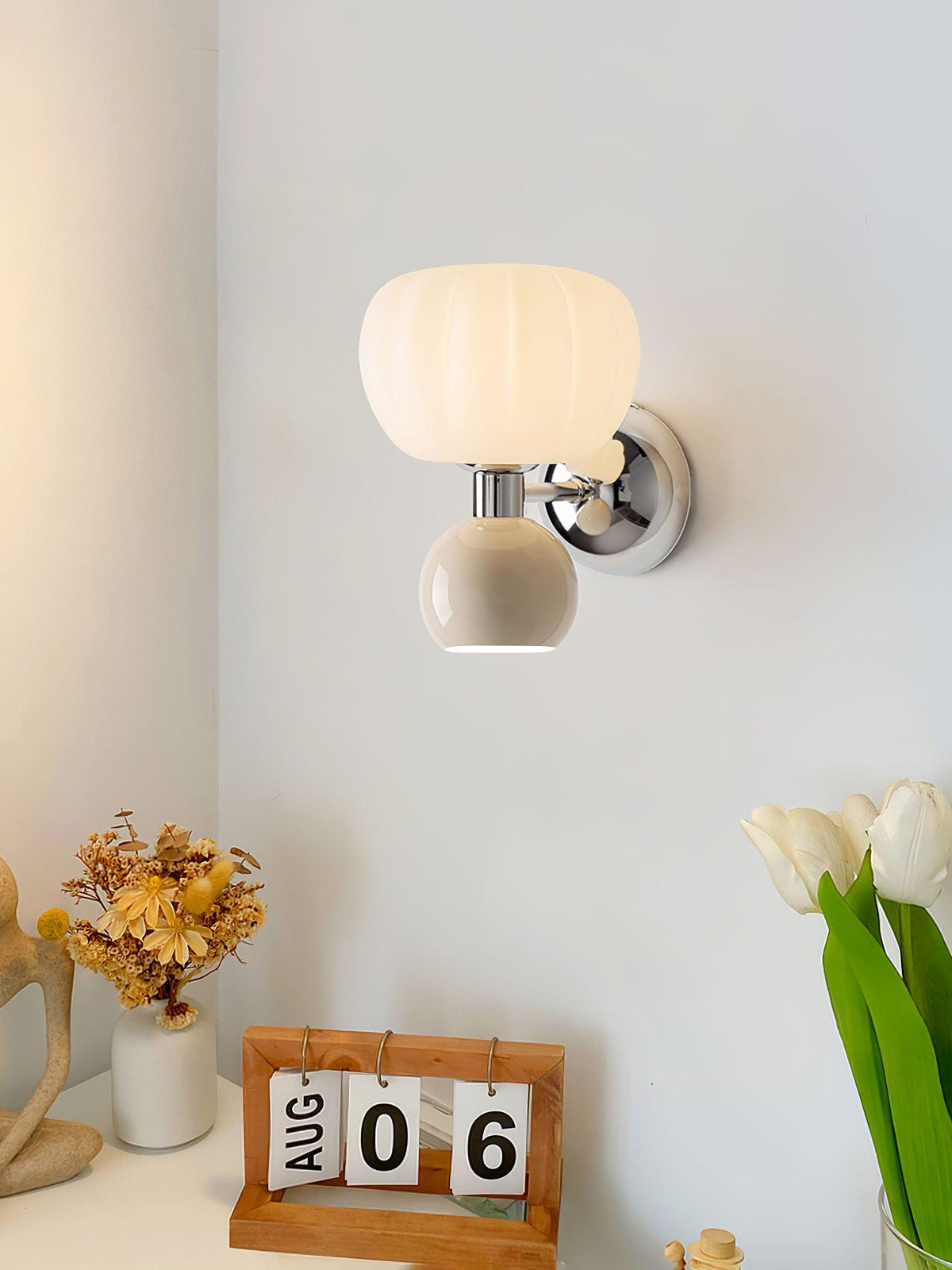 This Clérachic chrome wall light with a cream ball hangs above a desk with a flip calendar, dried flowers and white tulips.