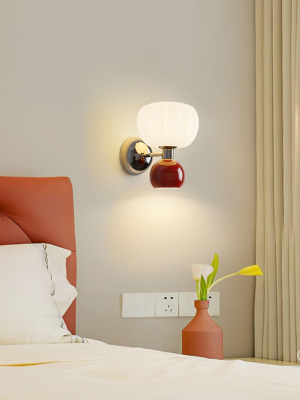 Over a bed with a terracotta headboard, this Clérachic chrome wall light with a deep red ball casts a warm pool of light down the wall.