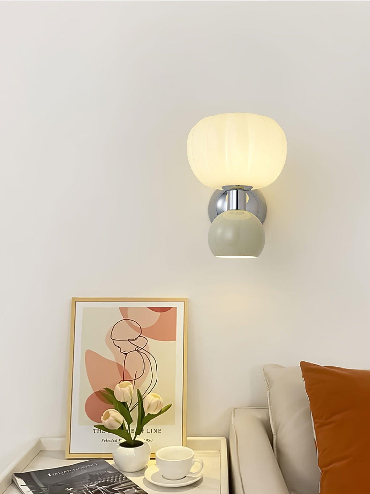 This Clérachic chrome wall light with a pale sage-grey ball hangs above a side table with a framed print and a cup of tea.