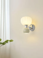 A Clérachic chrome wall sconce with a pale sage-grey ball glows beside a sheer curtain and a trailing green branch.