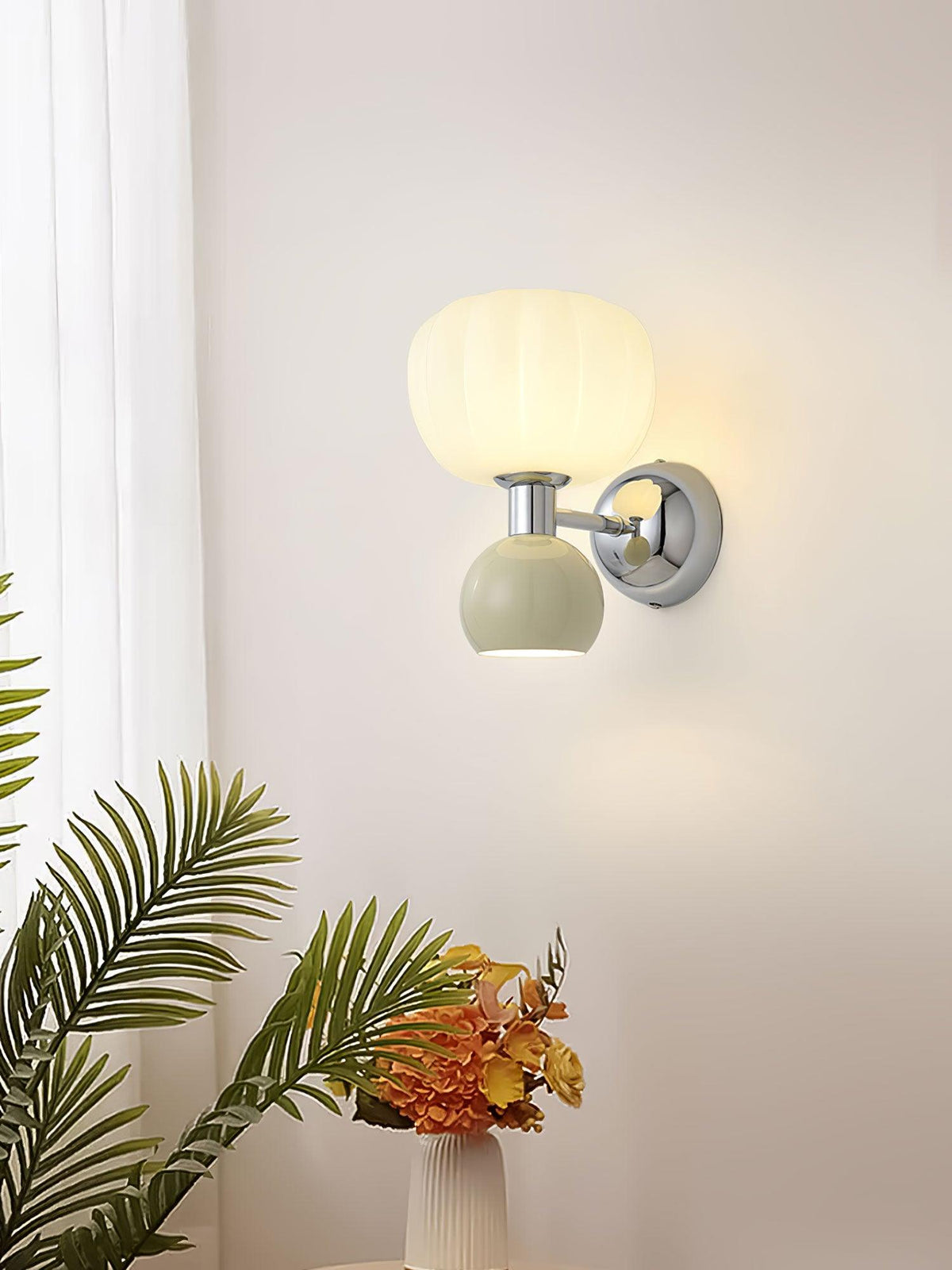 Lit next to a palm frond and a vase of orange flowers, this Clérachic chrome wall light has a pale sage-grey ball and a ribbed shade.
