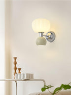 This Clérachic chrome wall light with a pale sage-grey ball sits above a thin wire shelf holding small cups and wooden ornaments.