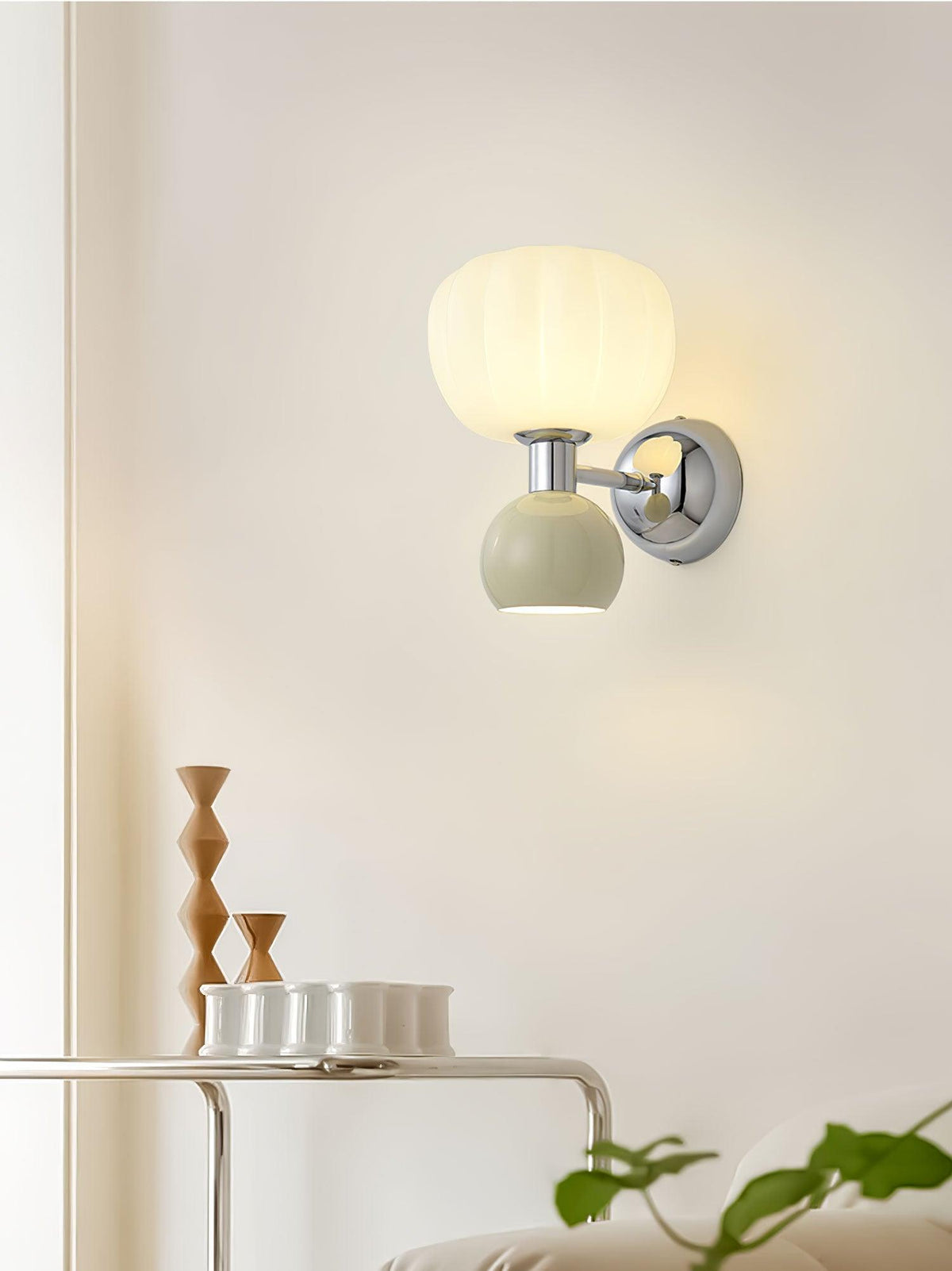 This Clérachic chrome wall light with a pale sage-grey ball sits above a thin wire shelf holding small cups and wooden ornaments.