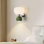 Over a white bed, this Clérachic chrome wall light with a dark green ball throws a warm cone of light down the wall.