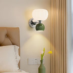 With a tan padded headboard and golden curtains behind, this Clérachic chrome wall light with a dark green ball glows above a vase of tulips.