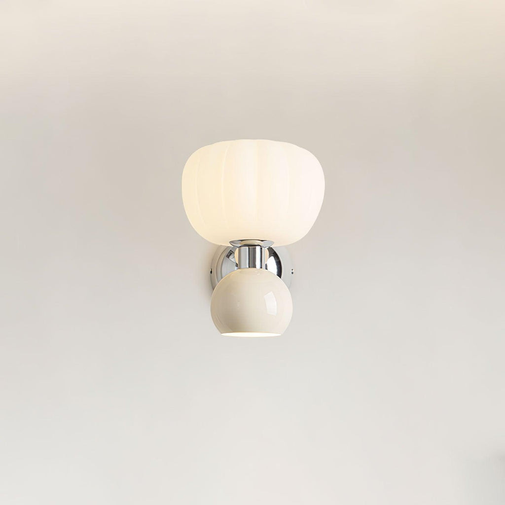 Straight-on view of this Clérachic chrome wall light with a cream ball and ribbed glass shade, lit on a plain pale wall.
