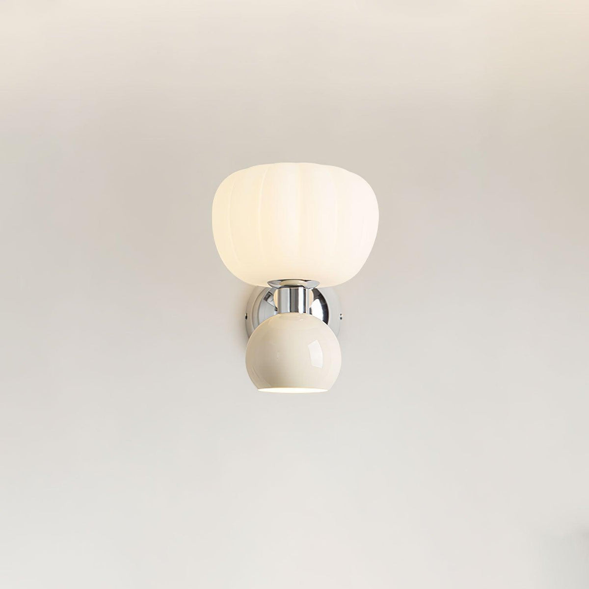Straight-on view of this Clérachic chrome wall light with a cream ball and ribbed glass shade, lit on a plain pale wall.