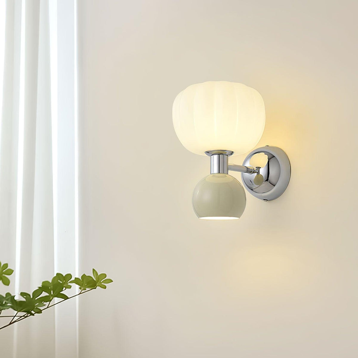 This Clérachic chrome wall light with a pale sage-grey ball glows next to a sheer white curtain and a green branch.