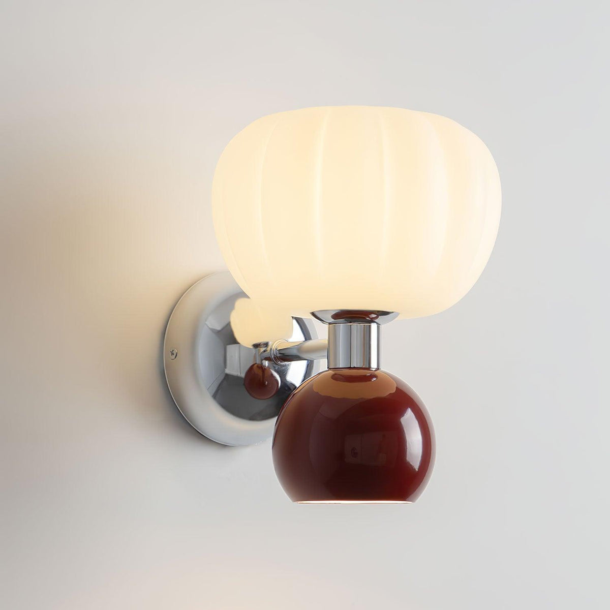 Close view of this Clérachic chrome wall light with a deep red ball and glossy chrome back plate under a ribbed glass shade.