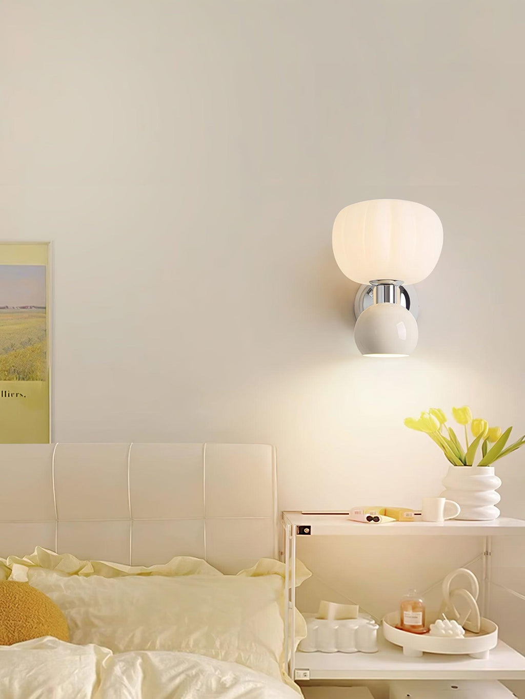A Clérachic chrome wall light with a cream ball lit above a bed with butter-yellow bedding and a shelf of small ornaments.