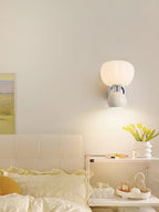 A Clérachic chrome wall light with a cream ball lit above a bed with butter-yellow bedding and a shelf of small ornaments.