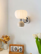 A Clérachic chrome wall light with a cream ball beside a desk calendar, dried flowers and white tulips on a white shelf.