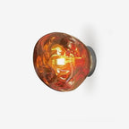 A Clérachic wall light with a melted-glass shade in a copper-toned finish, lit from within, on a plain white backdrop.