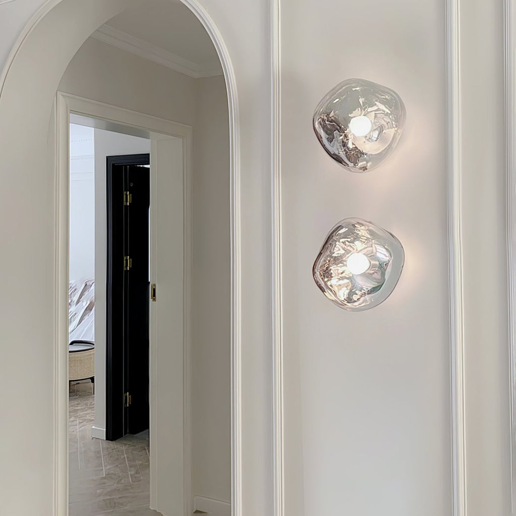 Two Clérachic wall lights with clear, melted-glass shades, stacked on a white wall beside an arched doorway.
