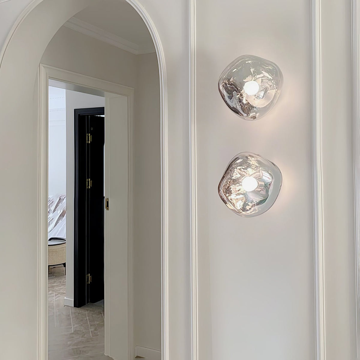 Two Clérachic wall lights with clear, melted-glass shades, stacked on a white wall beside an arched doorway.