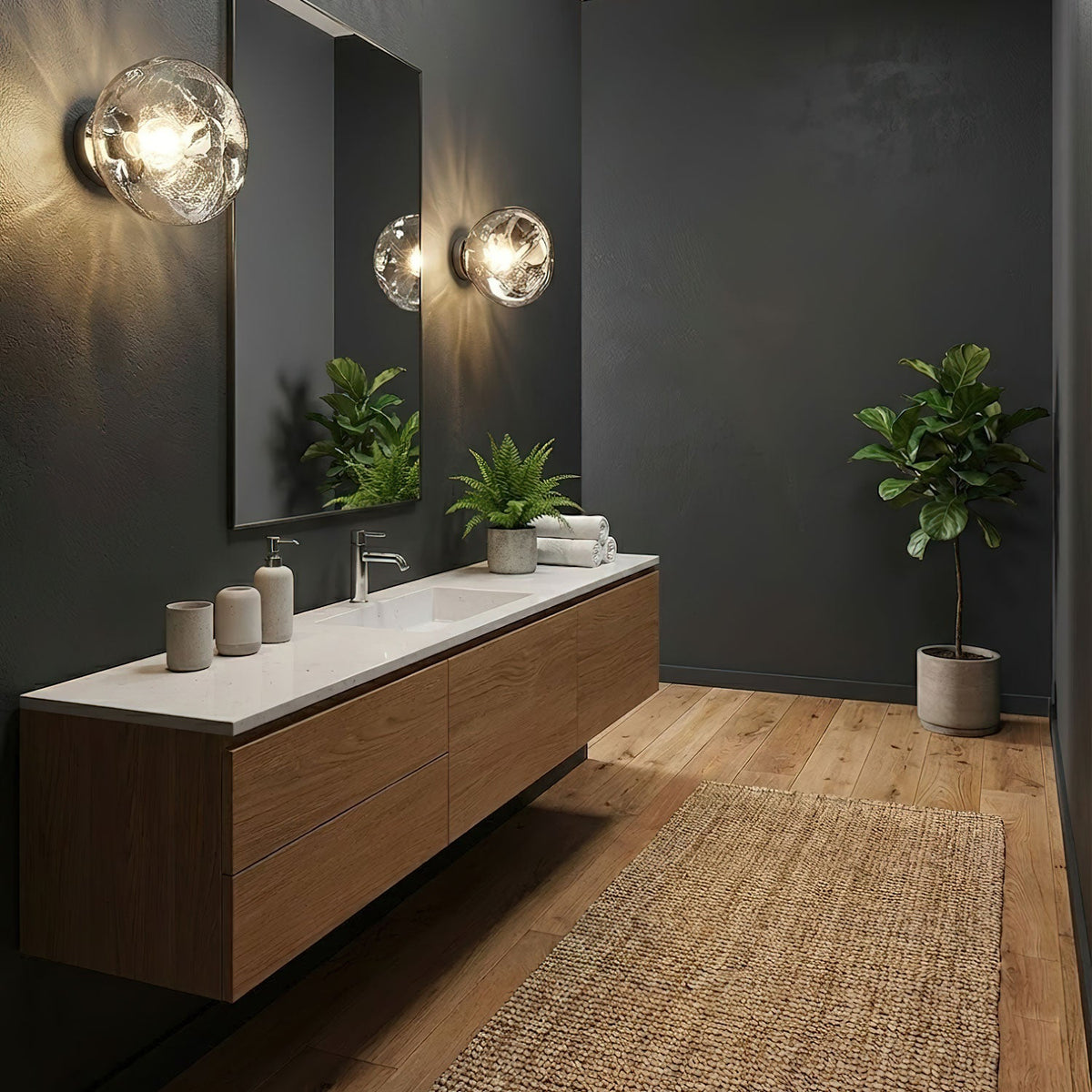 Two Clérachic wall lights with clear glass shades sit on a charcoal wall above a walnut vanity with a white top and mirror.