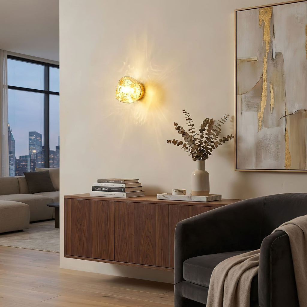 A lit gold-toned Clérachic wall light hangs above a walnut sideboard in a room with a big abstract painting and a city view.