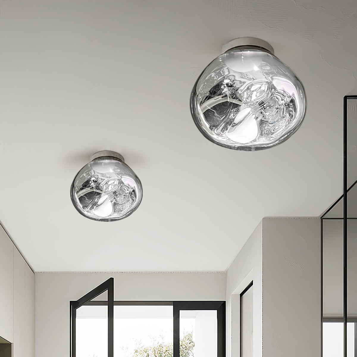 Two Clérachic ceiling-mounted lights in a mirror-silver finish, in different sizes, above a hallway with black-framed glazing.