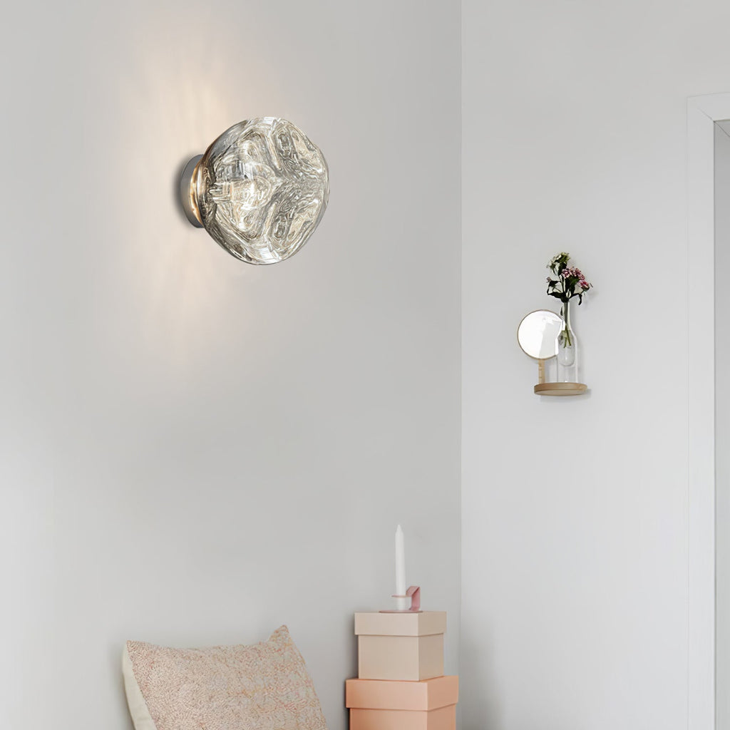 A Clérachic wall light with a clear, rippled-glass shade on a pale wall, with a small wall vase and a pastel cushion nearby.