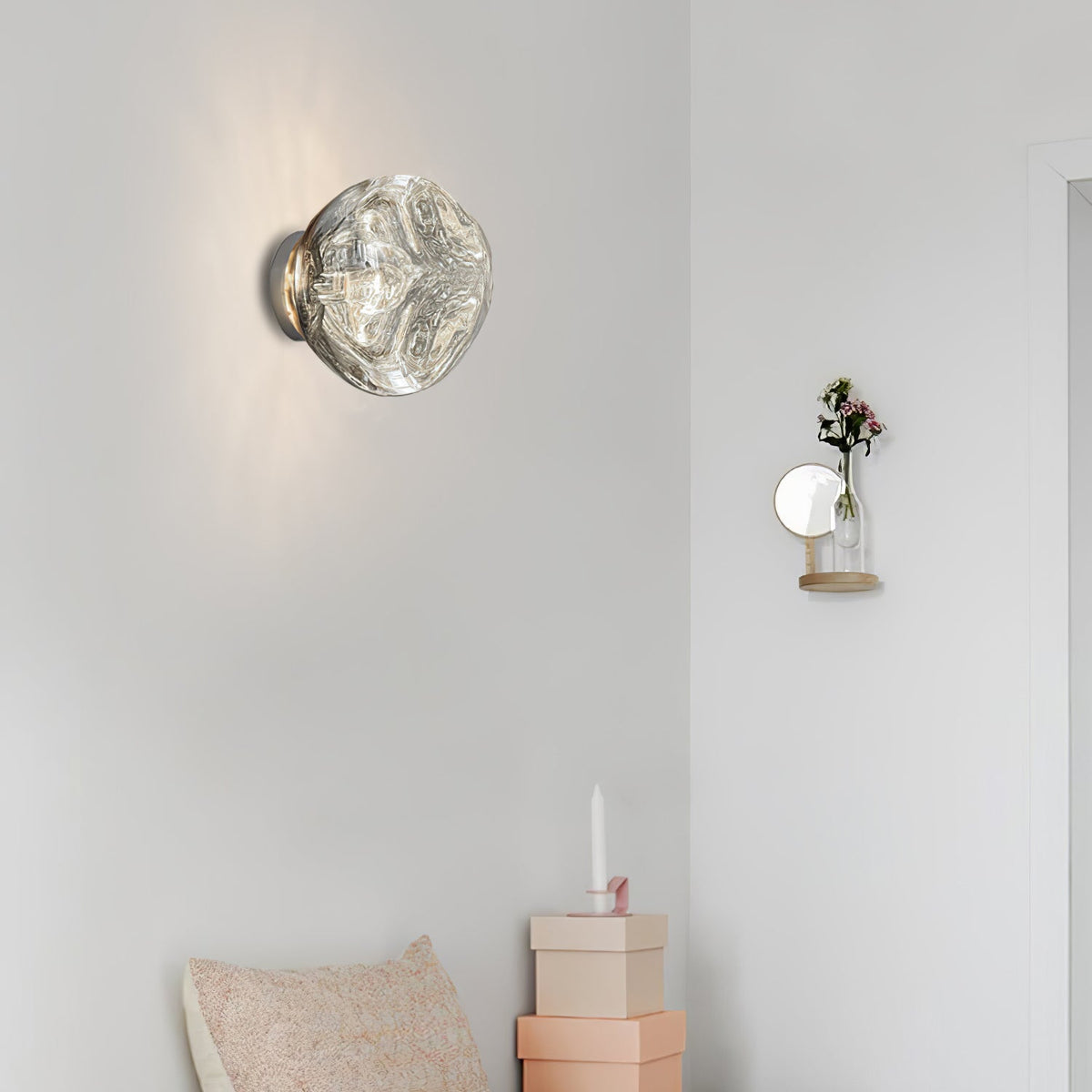 A Clérachic wall light with a clear, rippled-glass shade on a pale wall, with a small wall vase and a pastel cushion nearby.