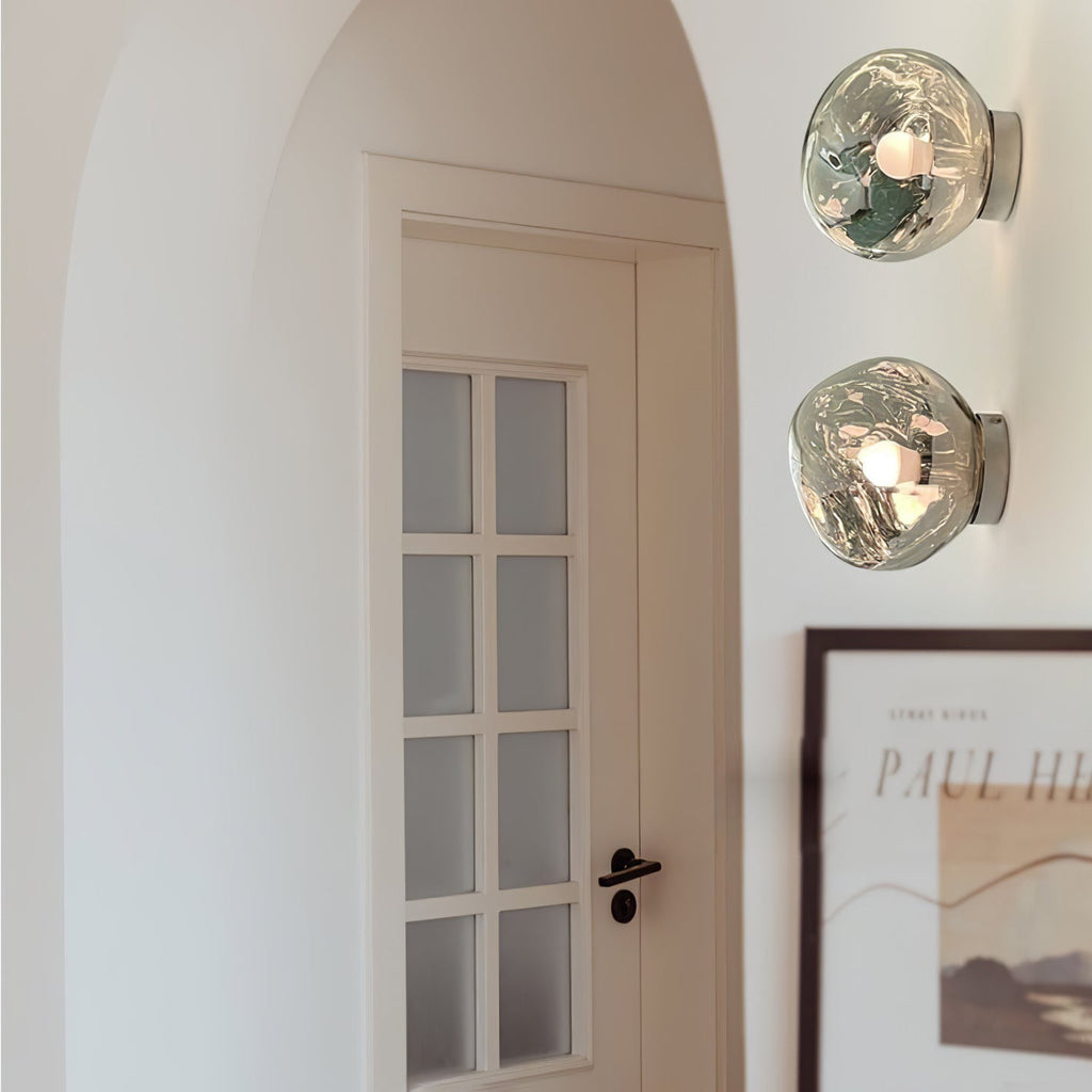 Two Clérachic wall lights with clear glass shades, stacked beside a panelled white door and a framed poster.