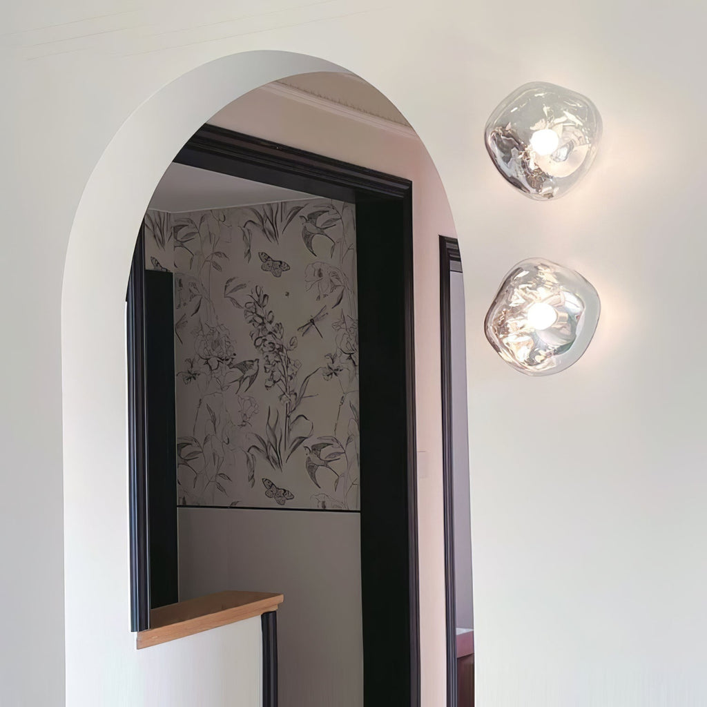 A pair of Clérachic wall lights with clear glass, mounted by a black-framed arched doorway with patterned wallpaper beyond.