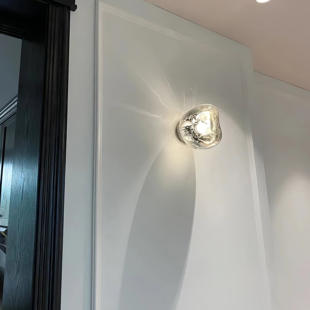 Glowing against a white wall with sweeping curved shapes, a Clérachic wall light shows a clear, melted-glass shade.