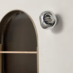 A silver, mirror-finish Clérachic wall light on a white wall beside an arched alcove with ribbed panelling.