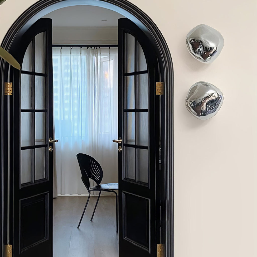 Two silver Clérachic wall lights beside black arched French doors, on a cream wall.