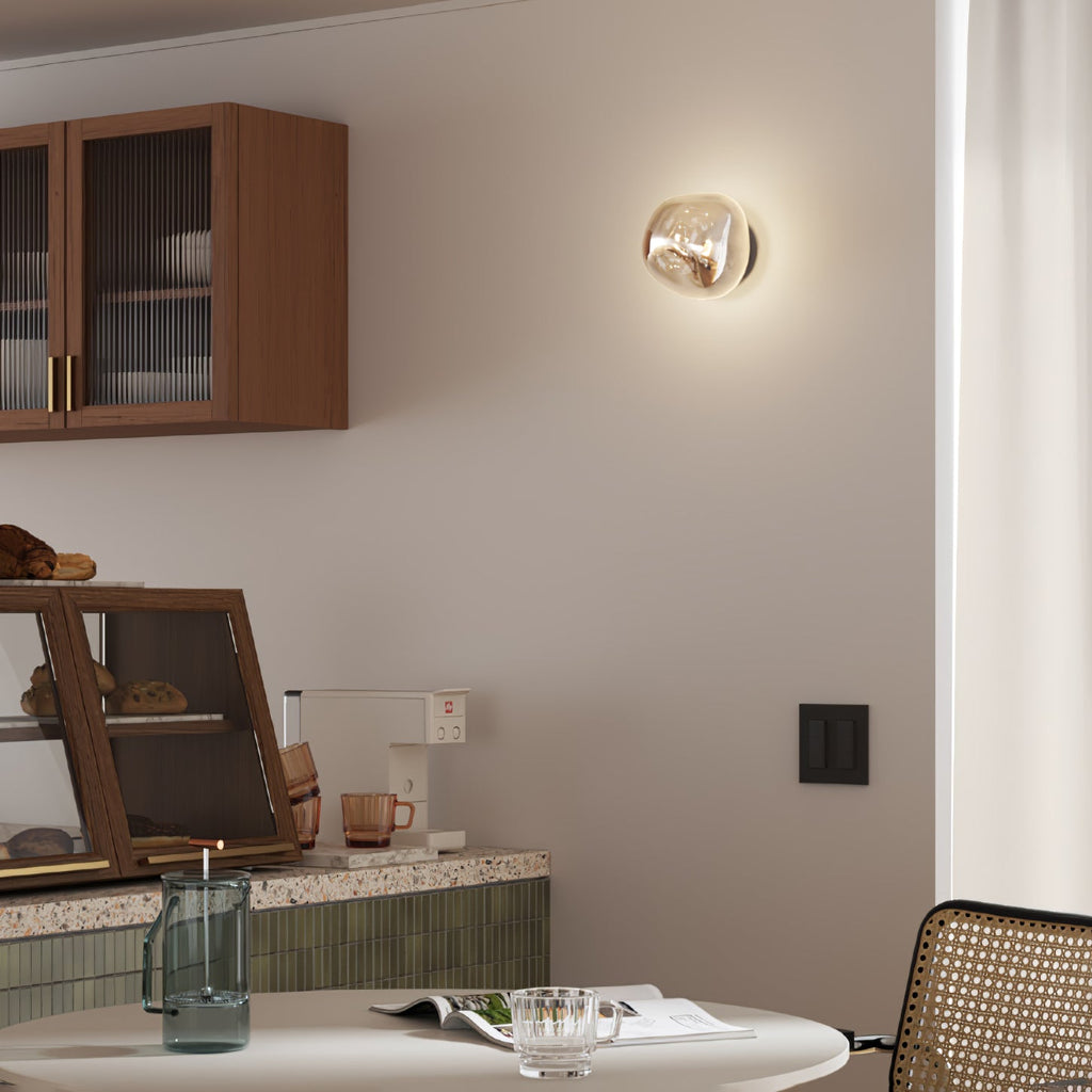 A lit Clérachic wall light with a champagne-toned glass shade, beside a wooden cabinet with ribbed glass doors.