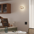 A lit Clérachic wall light with a champagne-toned glass shade, beside a wooden cabinet with ribbed glass doors.