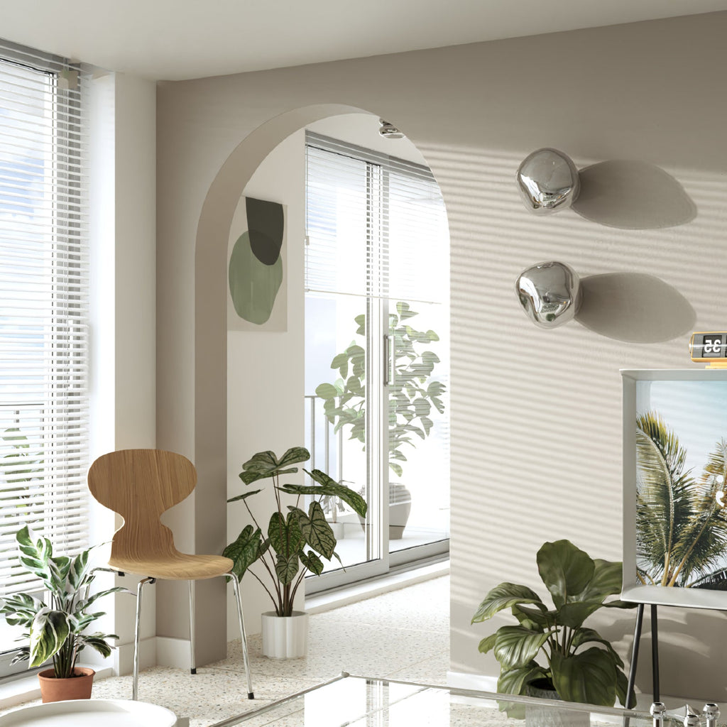 Silver Clérachic wall lights stacked on a ribbed beige wall in a room with an arched opening, plants and a wooden chair.