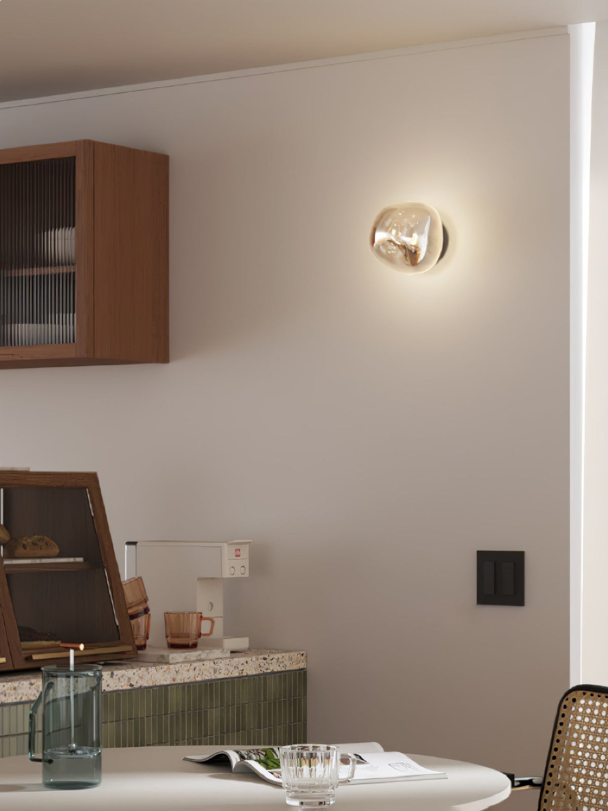 A Clérachic wall light with a champagne-toned glass shade, lit beside a wooden cabinet and above a kitchen counter.