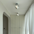 Two Clérachic ceiling lights with clear glass shades, hung along a corridor with white curtains and built-in cupboards.