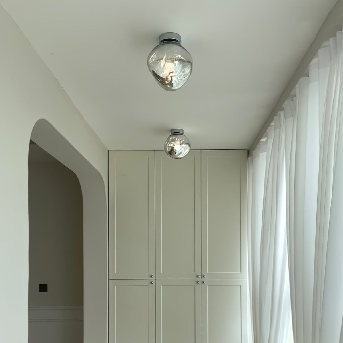 Two Clérachic ceiling lights with clear glass shades, hung along a corridor with white curtains and built-in cupboards.