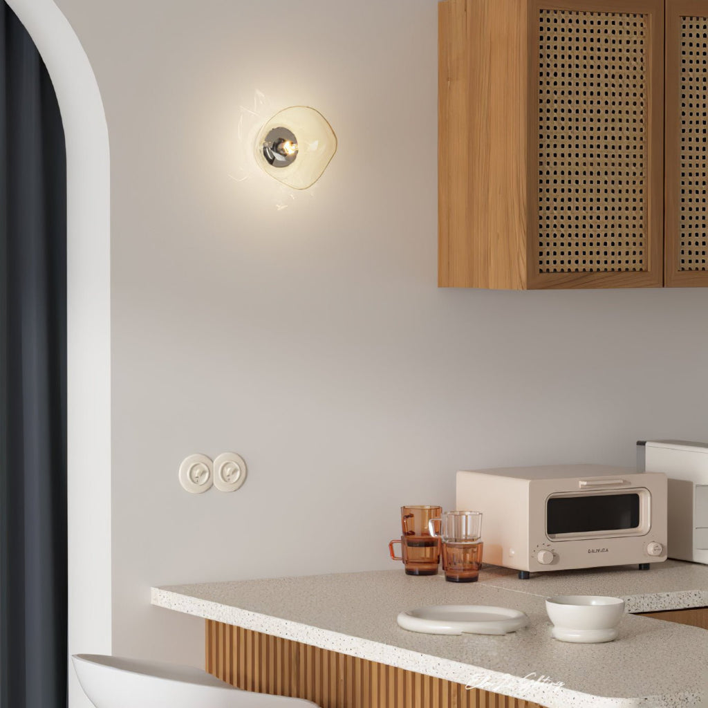 A Clérachic wall light with a clear, rounded glass shade over a kitchen counter, with a cane-fronted cabinet and a toaster.