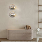 Two stacked Clérachic wall lights with clear, silver-tinted glass above a ribbed cream sideboard with a small elephant figure.