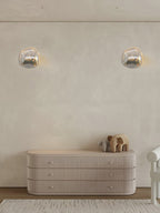 Two Clérachic wall lights set apart on a cream plaster wall, above a ribbed sideboard with an elephant figure.