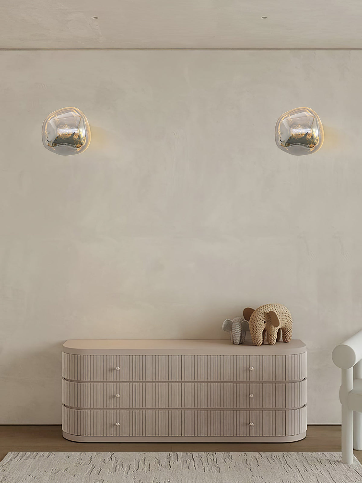 Two Clérachic wall lights set apart on a cream plaster wall, above a ribbed sideboard with an elephant figure.