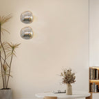 Two Clérachic wall lights with clear, silver-tinted glass beside a tall plant, with a bookcase and a round table below.