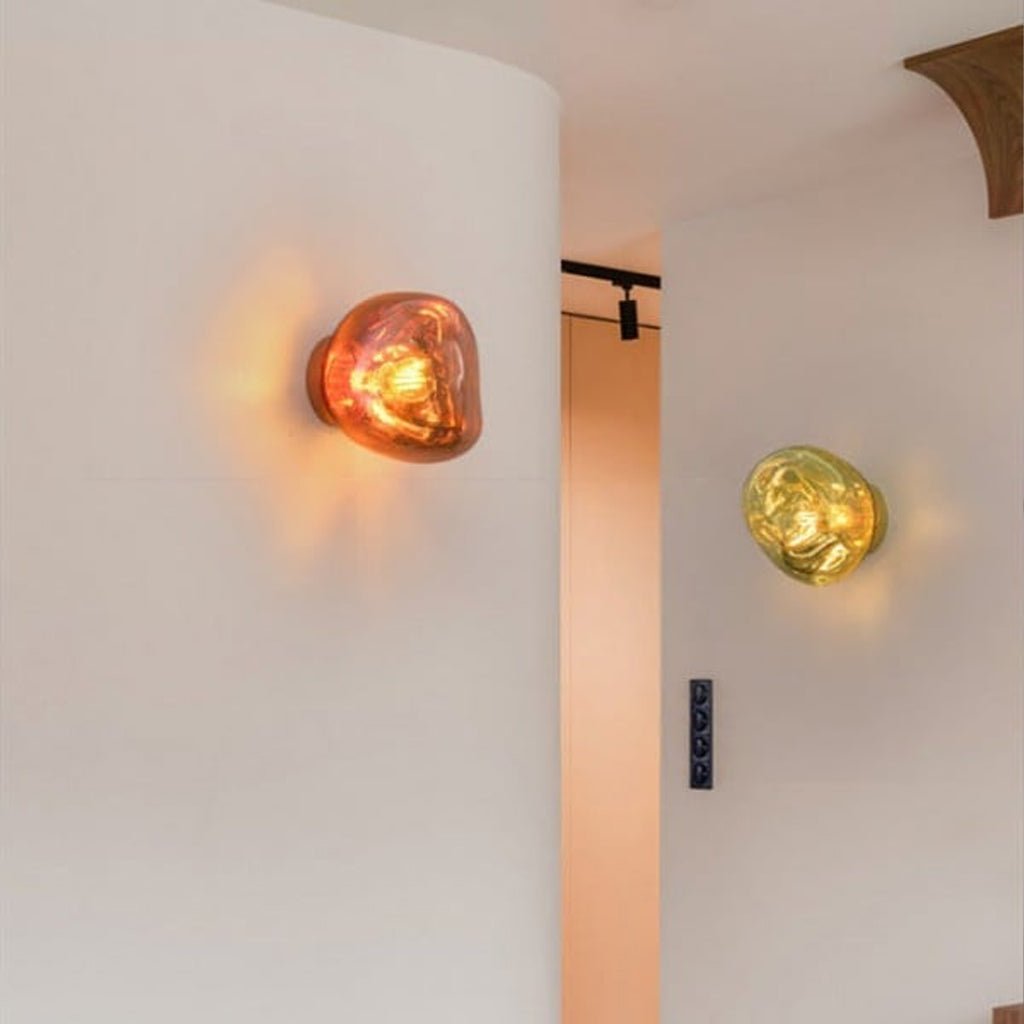 A lit Clérachic wall light on a curved white wall, with a copper-toned glow, and a second yellow-gold one beyond it.