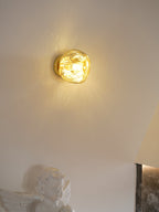 A gold Clérachic wall light lit beside a plaster cherub figure and a stone fireplace edge.