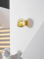 A small gold Clérachic wall light on a white wall, with a cherub figurine and a stepped light strip beyond.