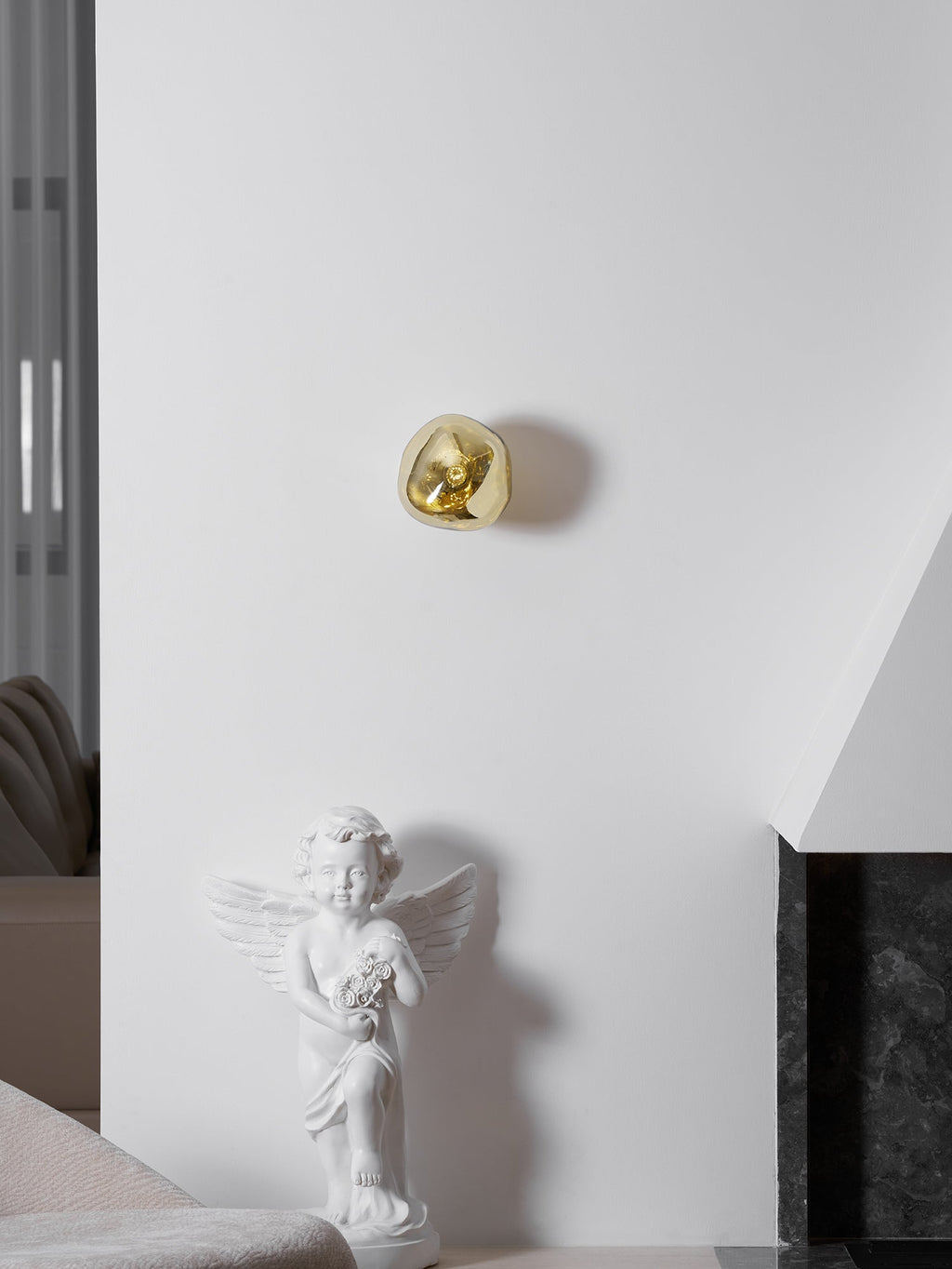 A small gold Clérachic wall light, high on a white wall above a cherub statue and a dark stone fireplace surround.