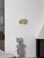 A small gold Clérachic wall light, high on a white wall above a cherub statue and a dark stone fireplace surround.
