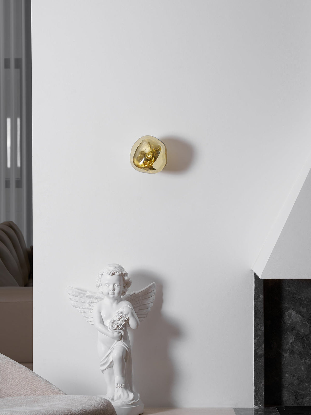 A small gold Clérachic wall light, high on a white wall above a cherub statue and a dark stone fireplace surround.