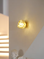 A gold Clérachic wall light glowing warm, with a lit staircase and a cherub figure at the left of the room.