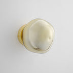 A gold Clérachic wall light with a smooth, pale glass shade, unlit, on a pale grey wall with a gold backplate.