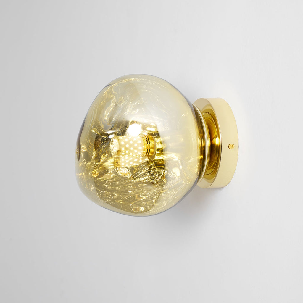 Side view of a Clérachic wall light with a gold-toned glass shade and a polished gold round backplate.