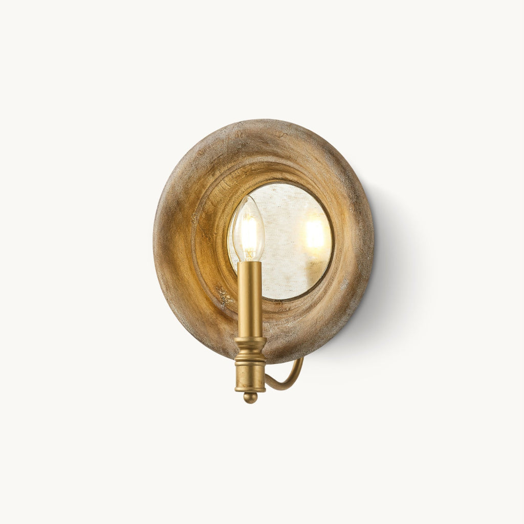 A Clérachic wall light with a round, weathered wood surround, a mirrored centre and a gold candle-style fitting, on a white backdrop.